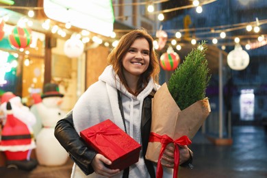 Photo of Happy woman with Christmas gift and thuja tree at fair