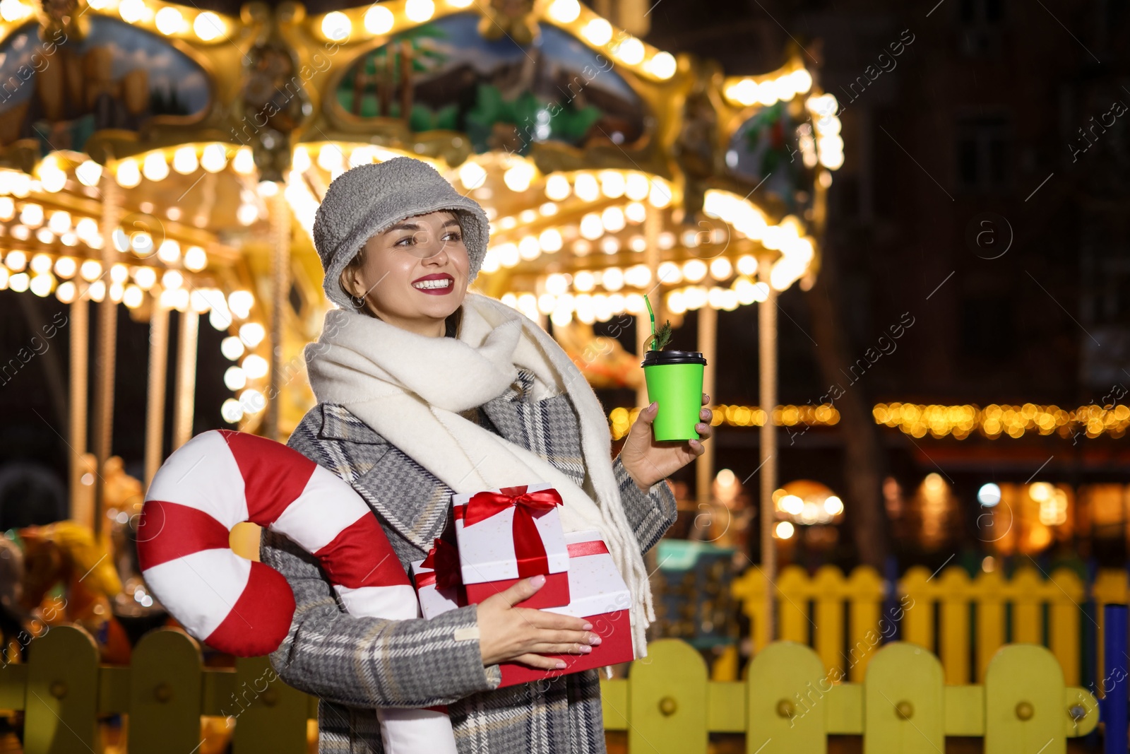 Photo of Happy woman with Christmas gifts and paper cup at funfair