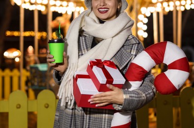 Photo of Happy woman with Christmas gifts and paper cup at funfair, closeup