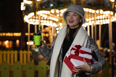 Photo of Happy woman with Christmas gifts and paper cup at funfair, space for text