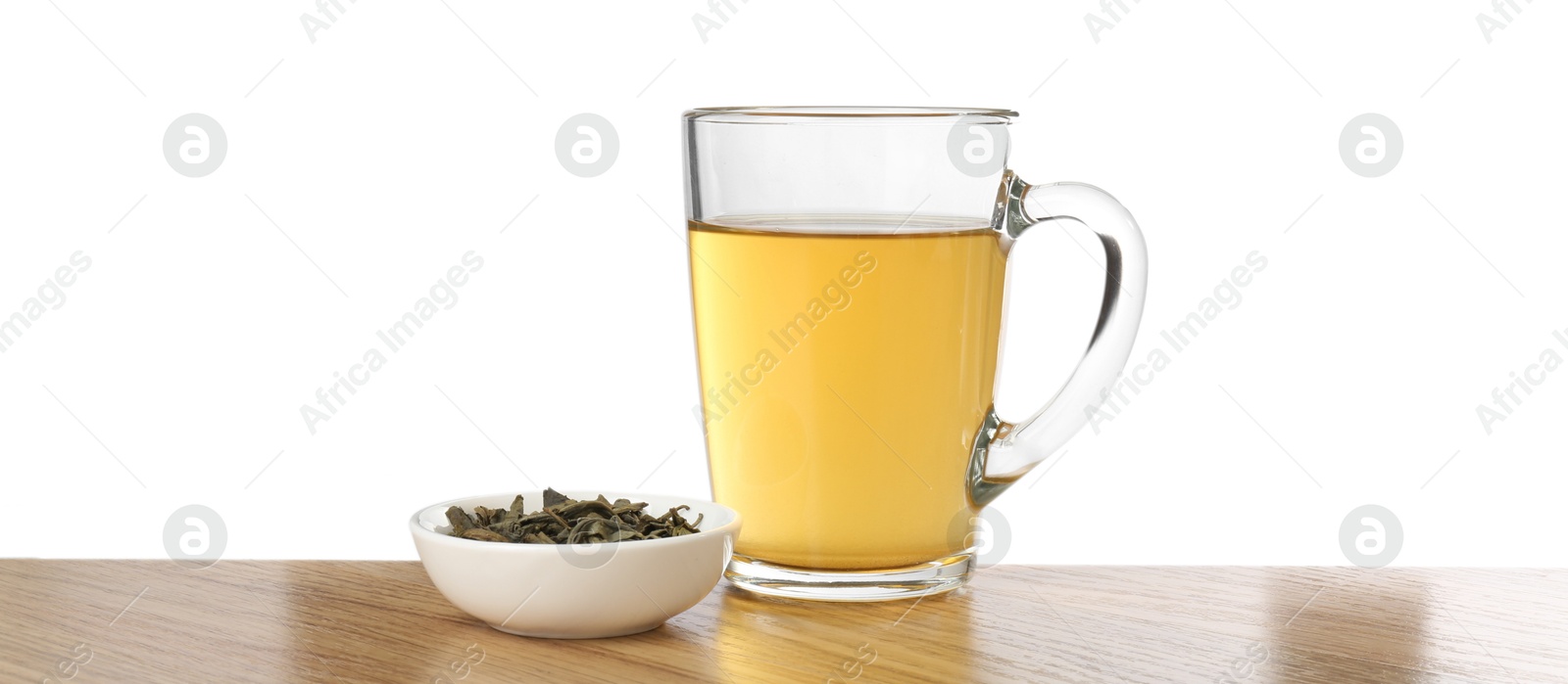 Photo of Refreshing green tea in cup and dry leaves on wooden table against white background