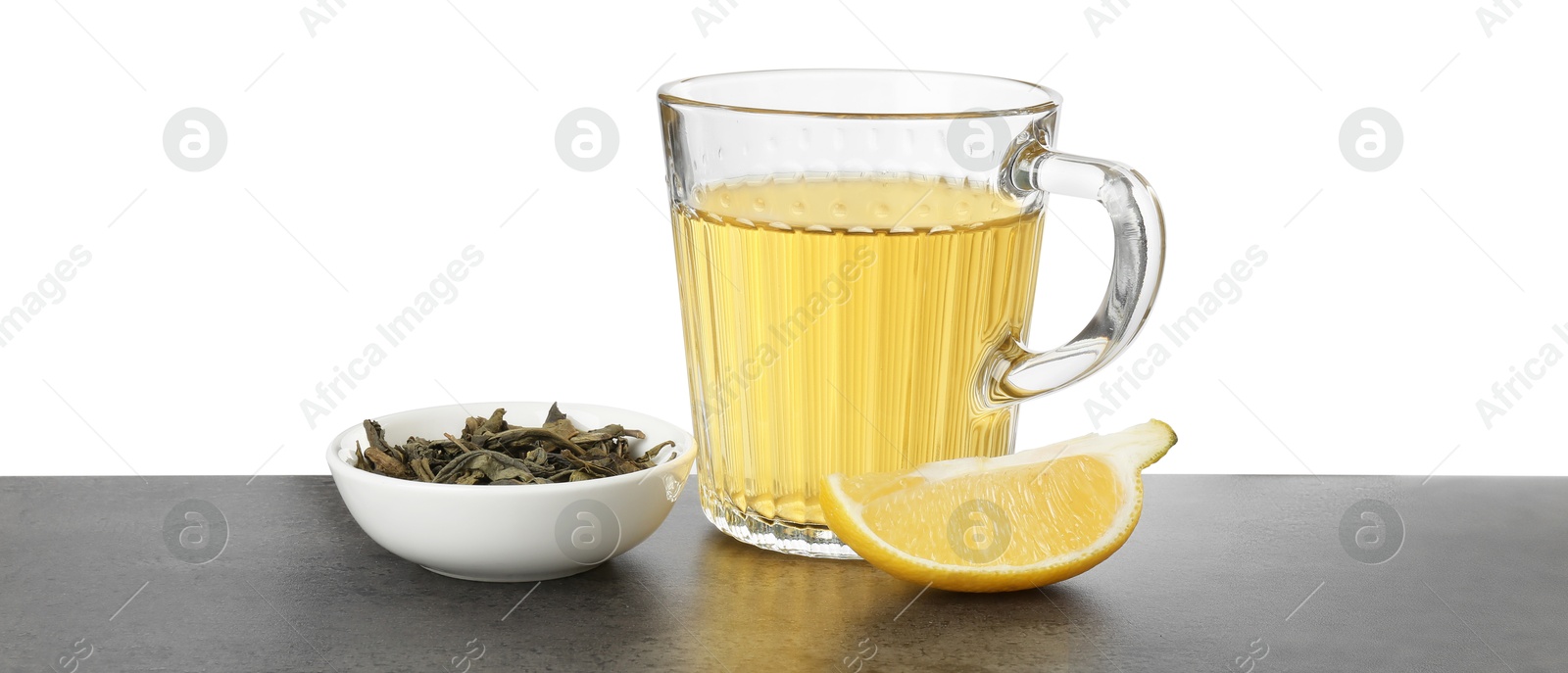 Photo of Refreshing green tea in cup, slice of lemon and dry leaves on grey textured table against white background