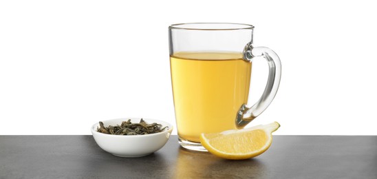 Photo of Refreshing green tea in cup, slice of lemon and dry leaves on grey textured table against white background