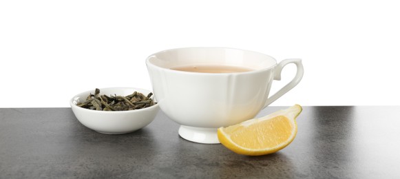 Photo of Refreshing green tea in cup, slice of lemon and dry leaves on grey textured table against white background