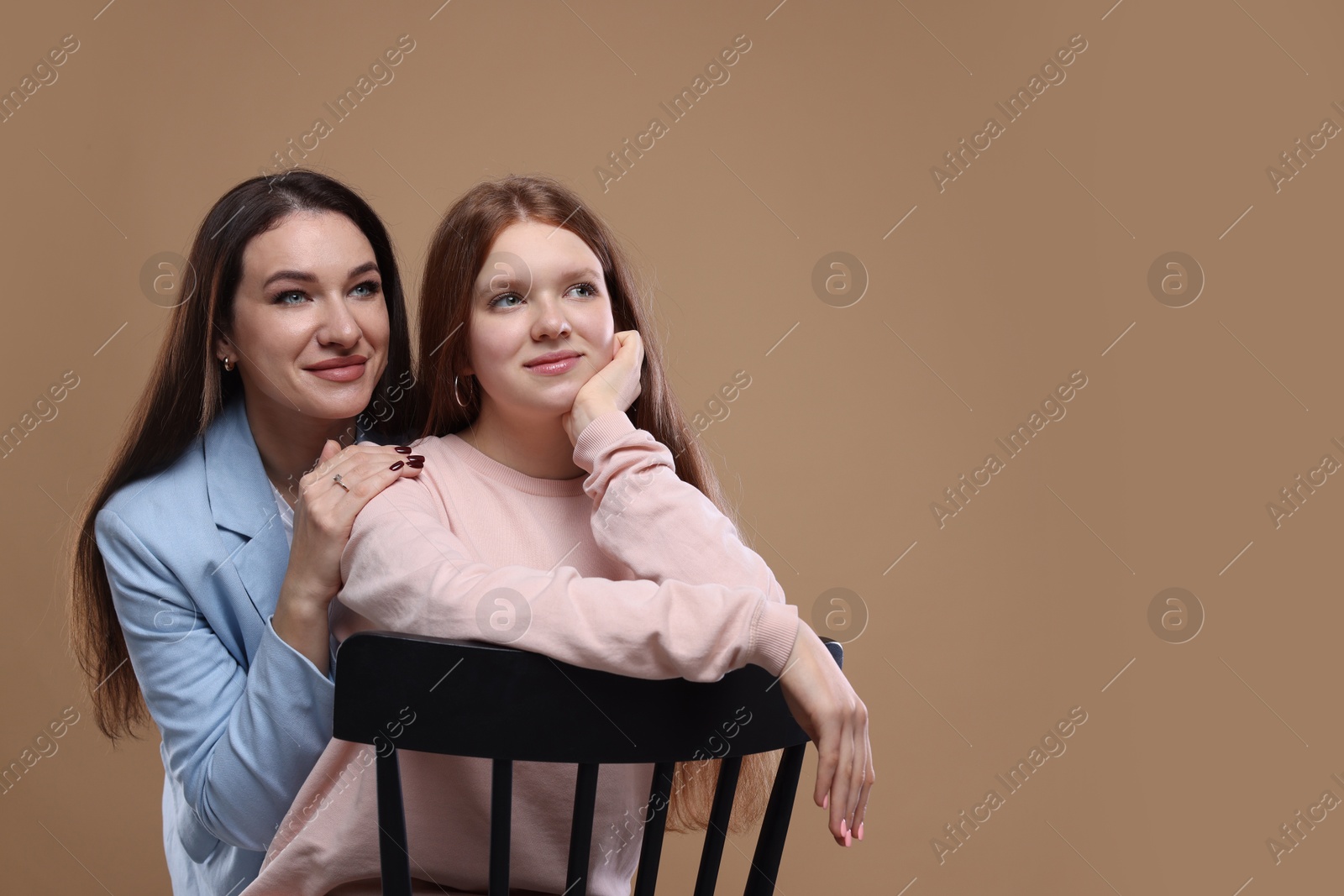 Photo of Portrait of beautiful mother with teenage daughter on dark beige background, space for text