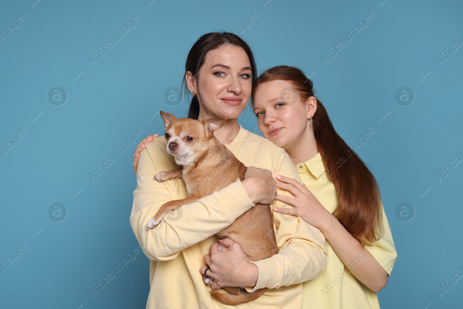 Photo of Portrait of beautiful mother with teenage daughter and cute Chihuahua dog on light blue background