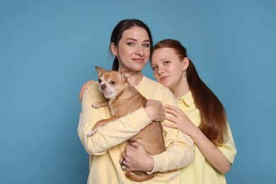 Photo of Portrait of beautiful mother with teenage daughter and cute Chihuahua dog on light blue background