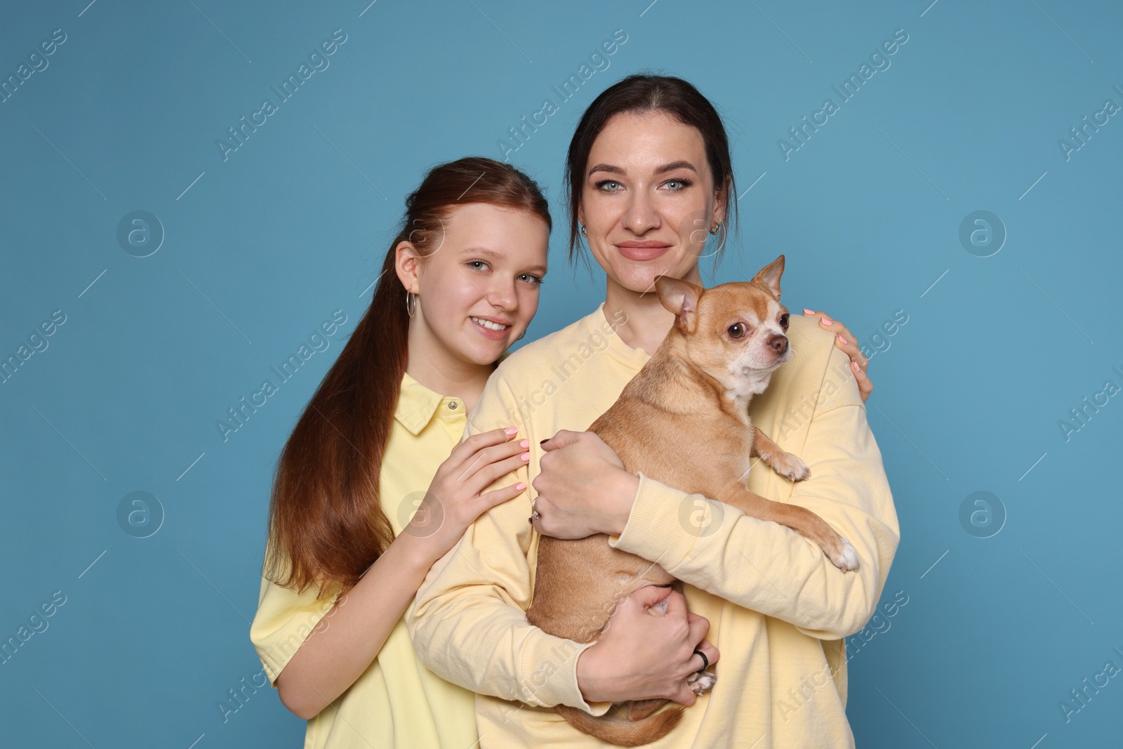 Photo of Portrait of beautiful mother with teenage daughter and cute Chihuahua dog on light blue background