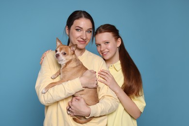 Photo of Portrait of beautiful mother with teenage daughter and cute Chihuahua dog on light blue background