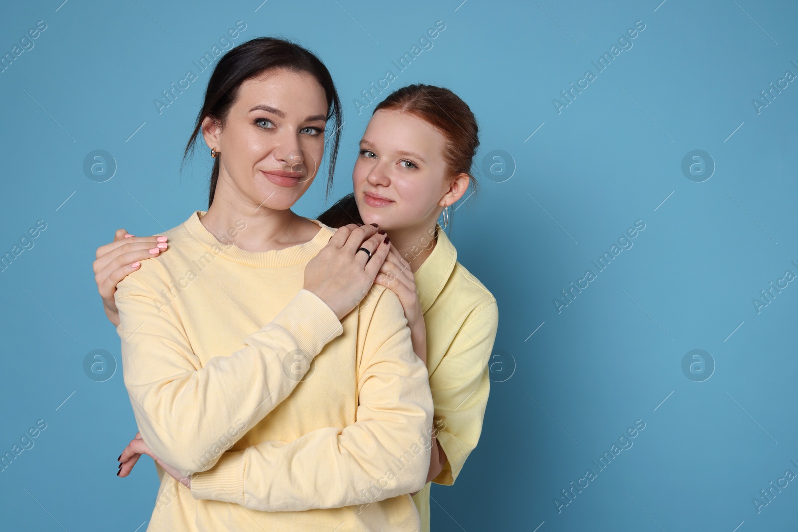 Photo of Portrait of beautiful mother with teenage daughter on light blue background, space for text