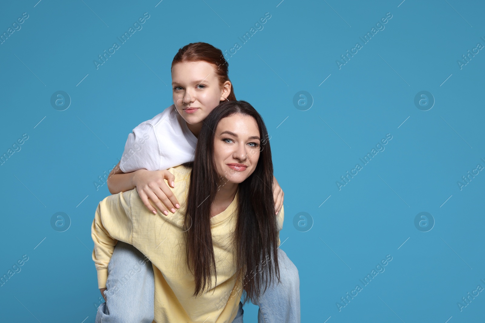 Photo of Portrait of beautiful mother with teenage daughter on light blue background, space for text