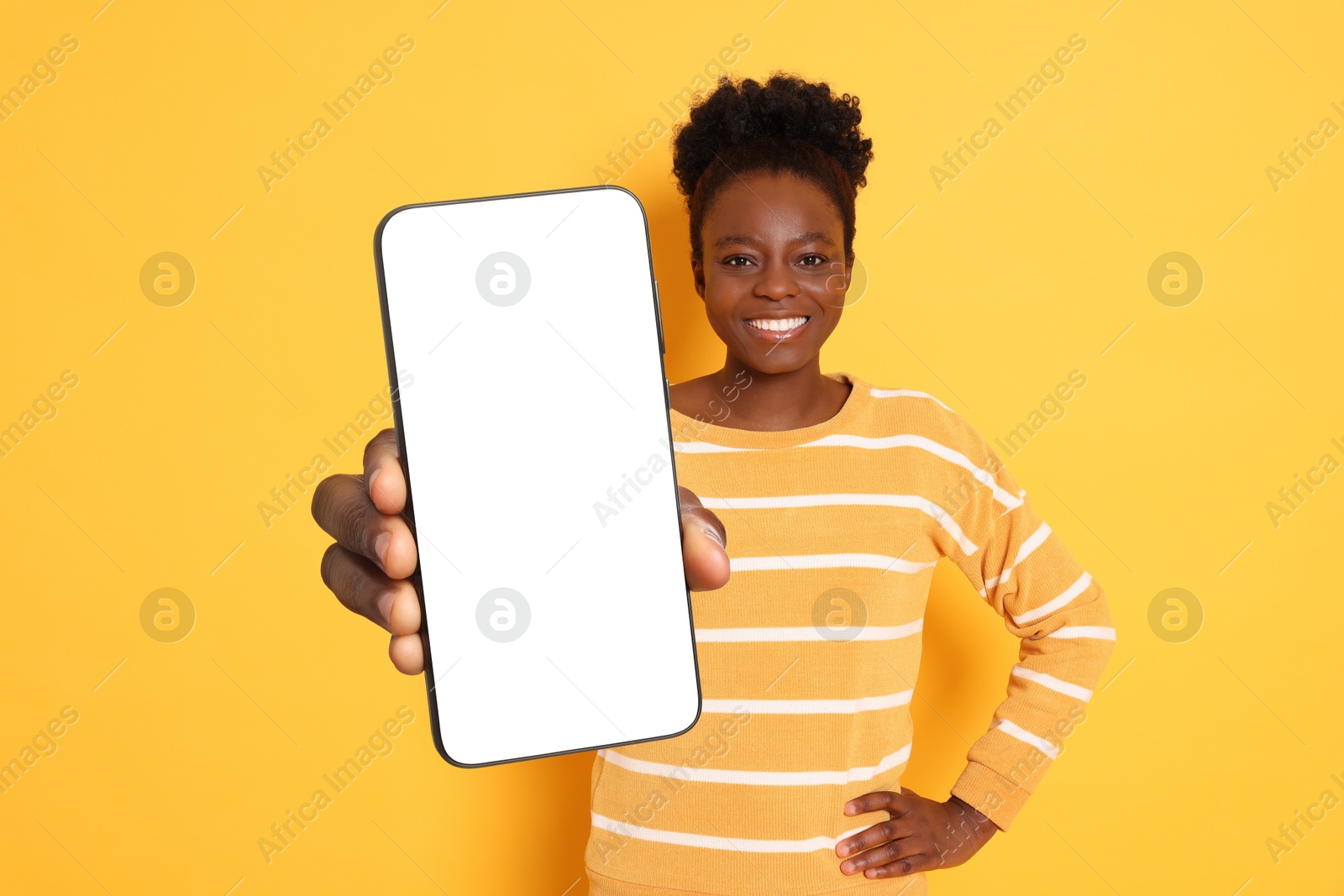 Image of Happy woman showing mobile phone with blank screen on orange background. Mockup for design