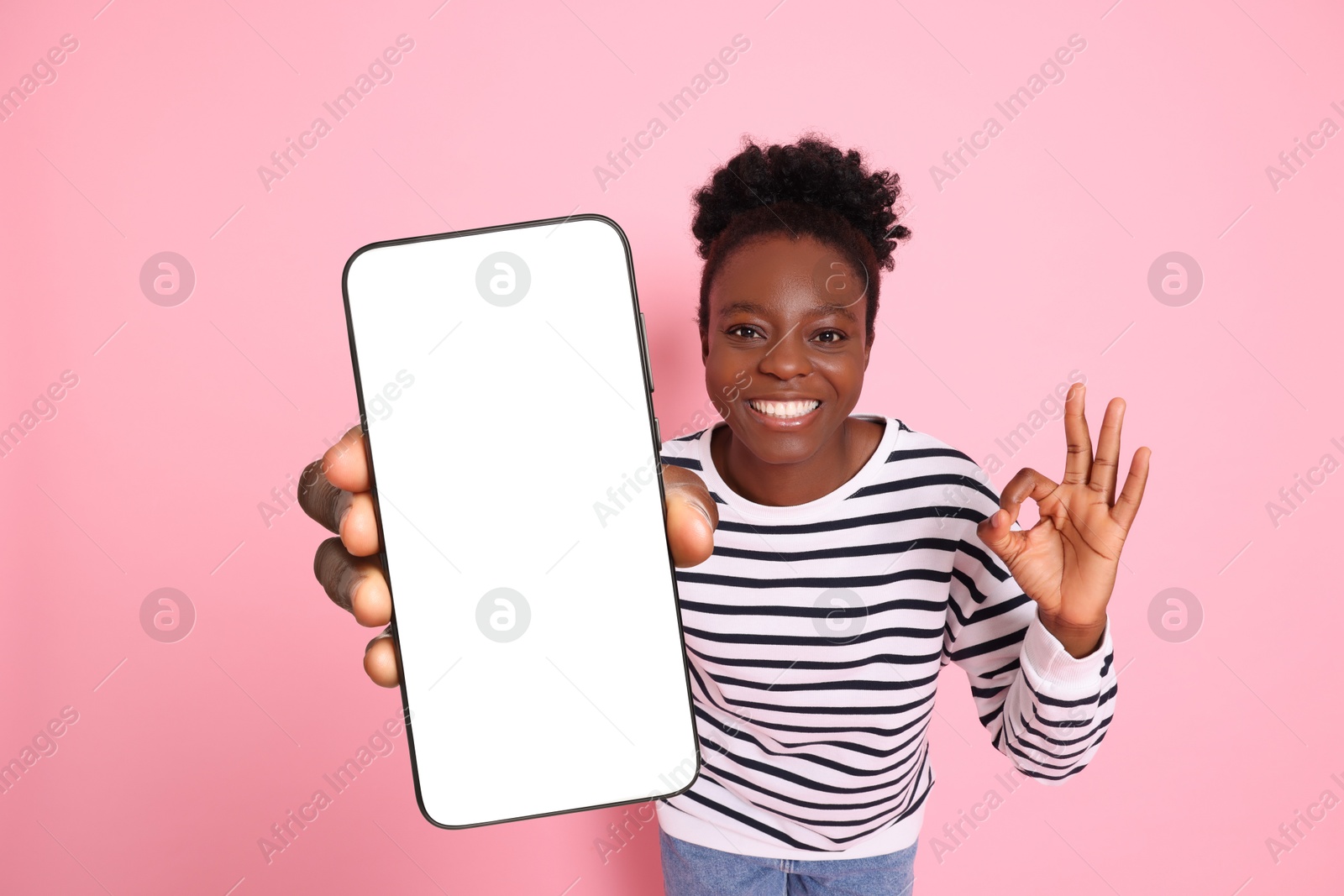 Image of Happy woman showing mobile phone with blank screen and gesture ok on pink background. Mockup for design