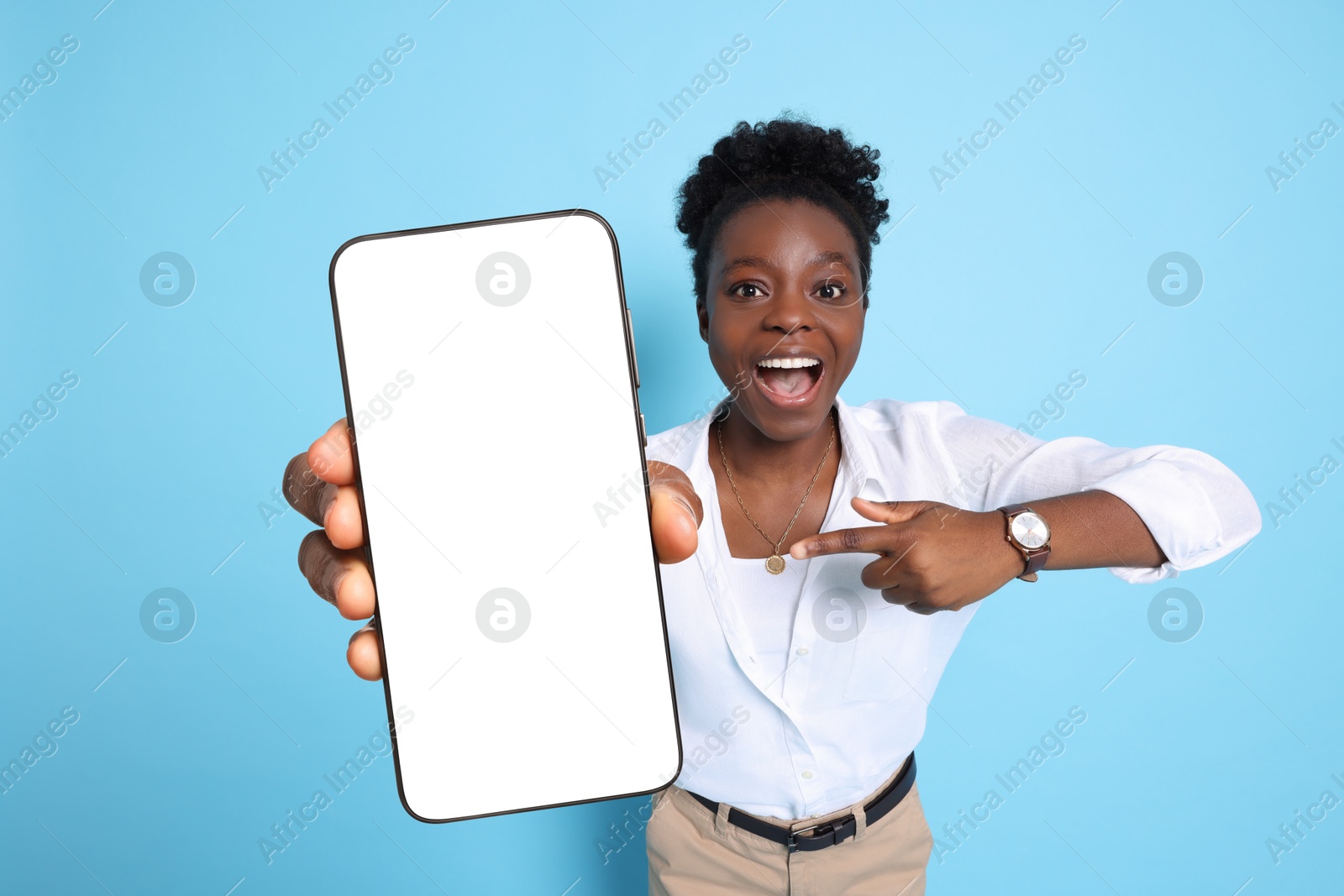 Image of Excited woman pointing at mobile phone with blank screen on light blue background. Mockup for design