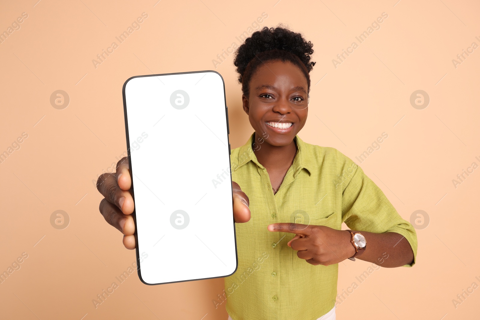 Image of Happy woman pointing at mobile phone with blank screen on beige background. Mockup for design