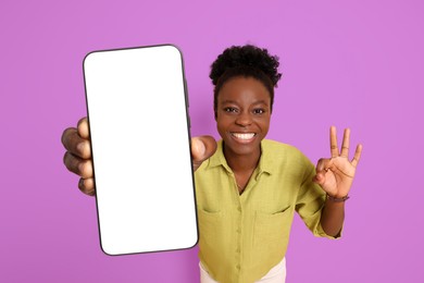 Image of Happy woman showing mobile phone with blank screen and gesture ok on violet background. Mockup for design