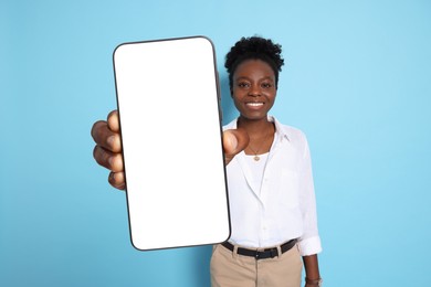 Image of Happy woman showing mobile phone with blank screen on light blue background. Mockup for design