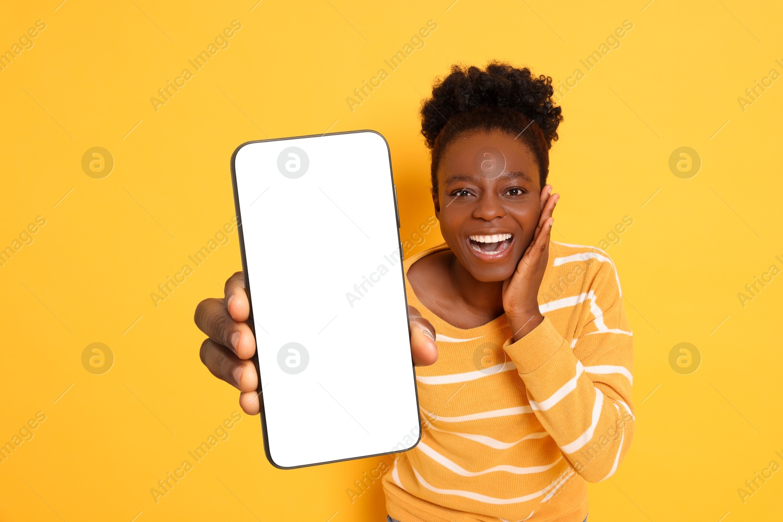 Image of Excited woman showing mobile phone with blank screen on orange background. Mockup for design