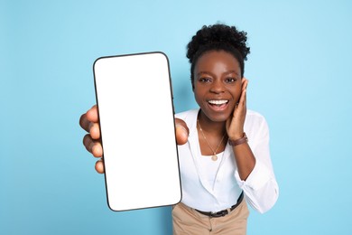 Image of Excited woman showing mobile phone with blank screen on light blue background. Mockup for design