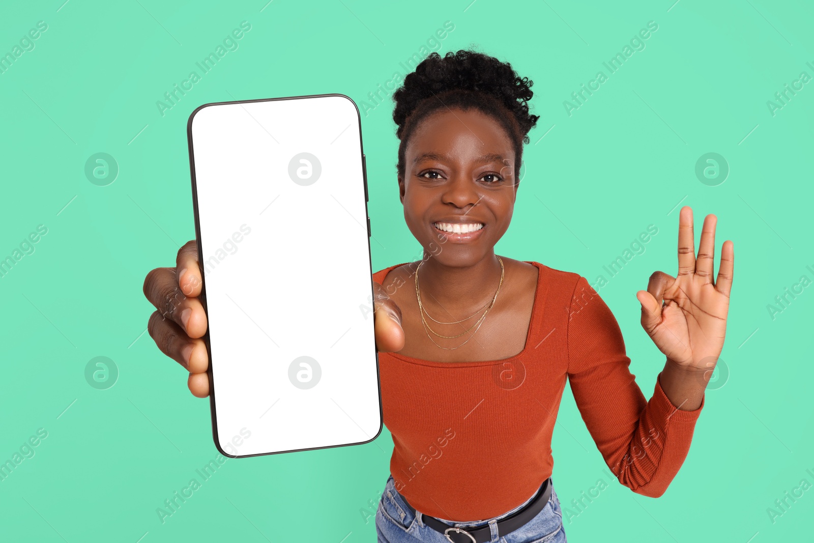 Image of Happy woman showing mobile phone with blank screen and gesture ok on turquoise background. Mockup for design