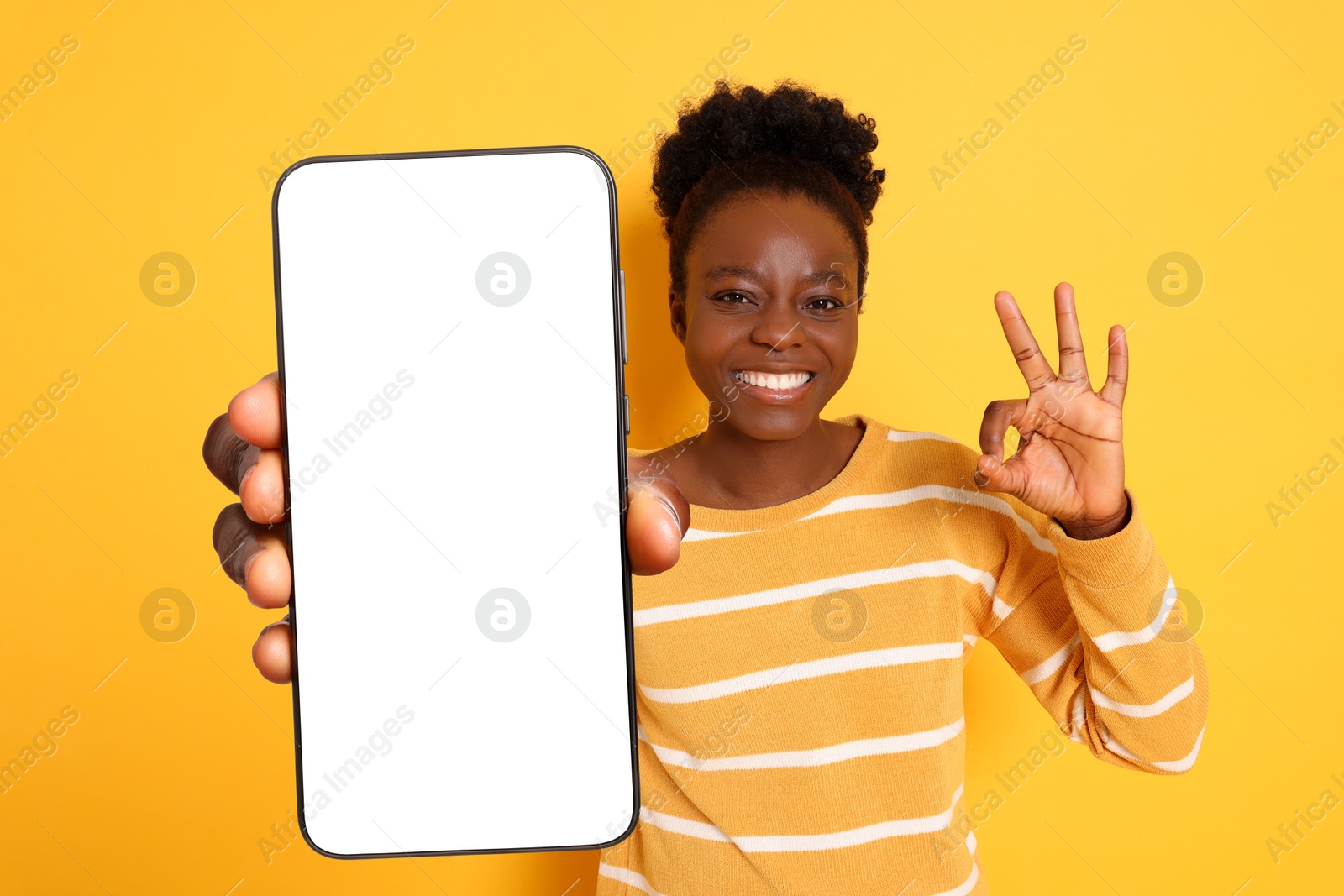 Image of Happy woman showing mobile phone with blank screen and gesture ok on orange background. Mockup for design