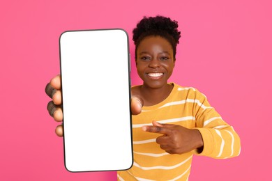 Image of Happy woman pointing at mobile phone with blank screen on pink background. Mockup for design