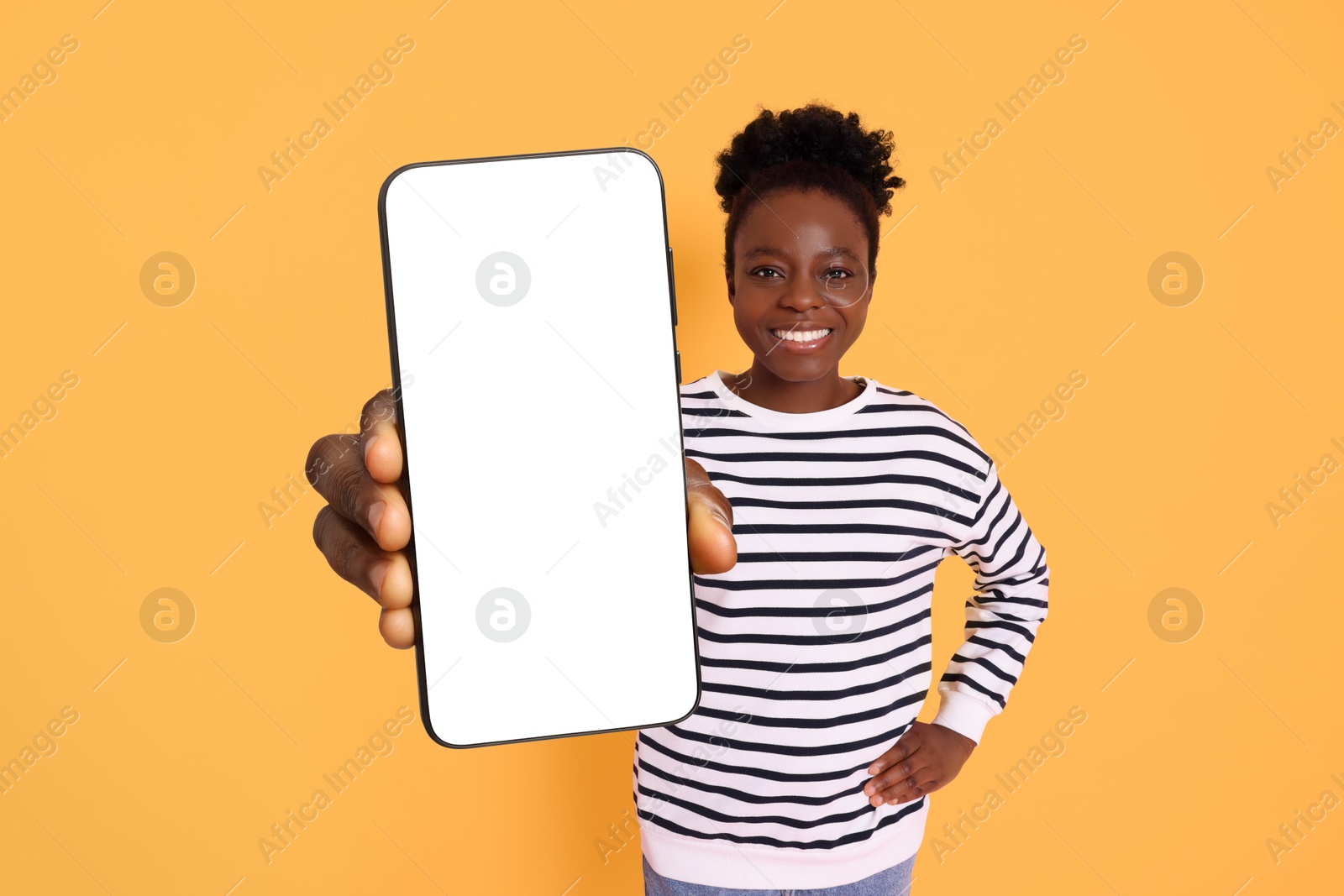 Image of Happy woman showing mobile phone with blank screen on orange background. Mockup for design