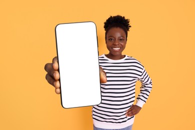 Image of Happy woman showing mobile phone with blank screen on orange background. Mockup for design