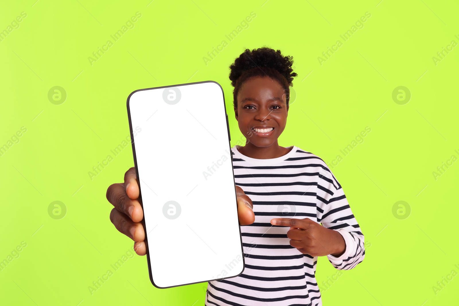 Image of Happy woman pointing at mobile phone with blank screen on lime color background. Mockup for design