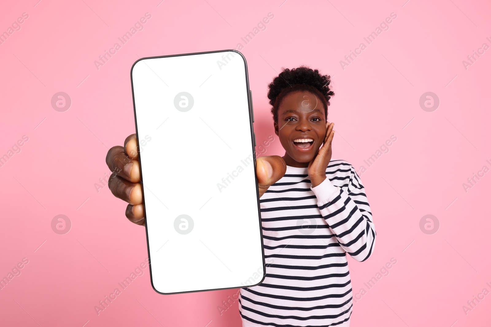 Image of Excited woman showing mobile phone with blank screen on pink background. Mockup for design