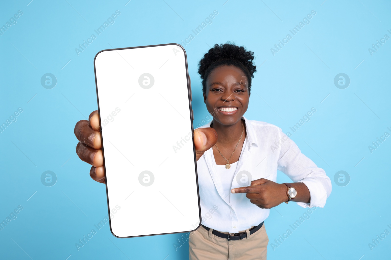 Image of Happy woman pointing at mobile phone with blank screen on light blue background. Mockup for design