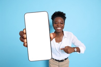 Image of Happy woman pointing at mobile phone with blank screen on light blue background. Mockup for design