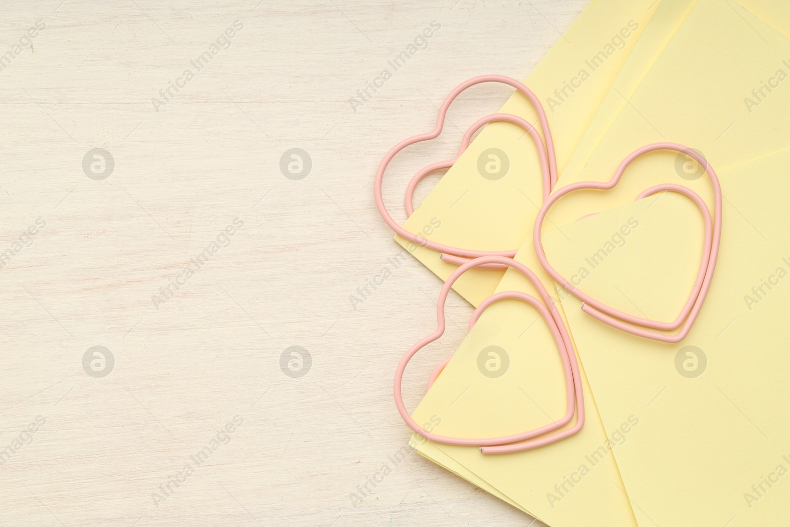 Photo of Heart shaped paper clips and notes on wooden table, top view. Space for text