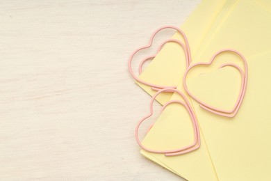 Photo of Heart shaped paper clips and notes on wooden table, top view. Space for text