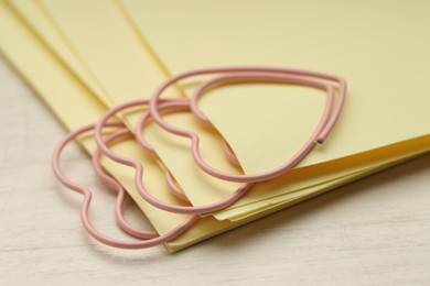 Photo of Heart shaped paper clips and notes on wooden table, closeup