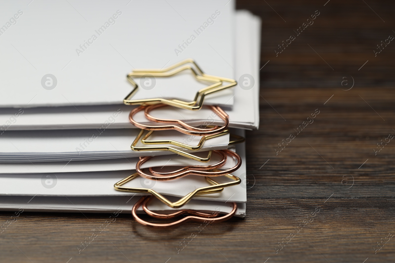 Photo of Metal paper clips and notes on wooden table, closeup. Space for text