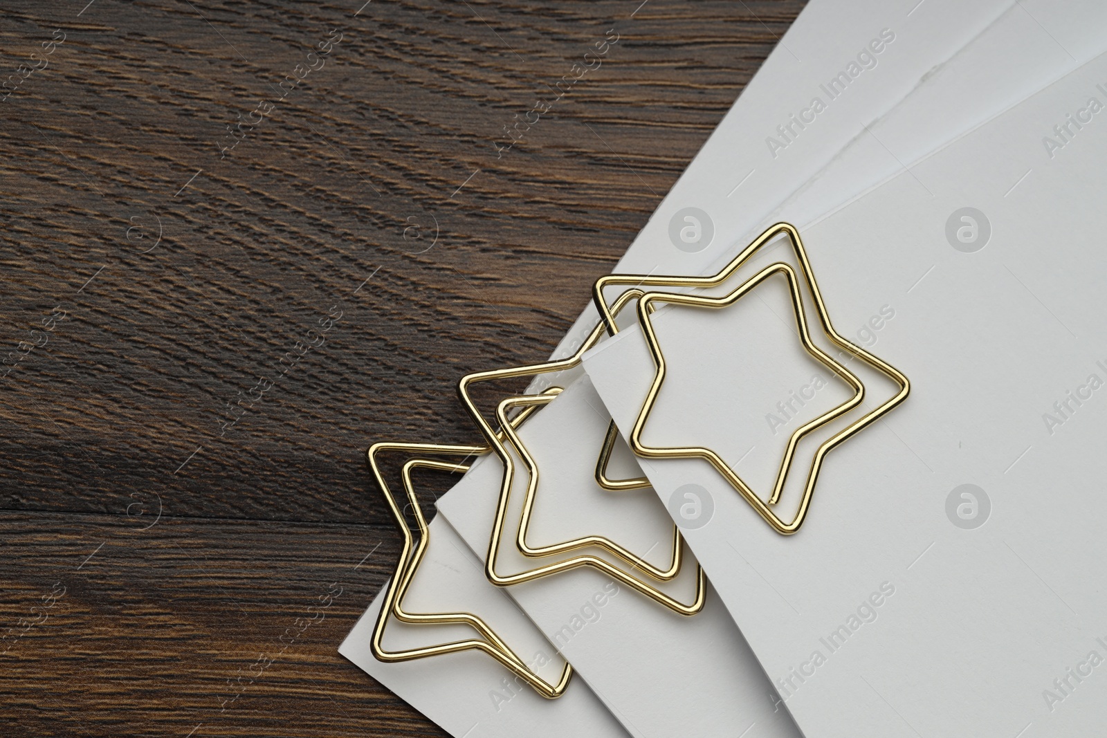 Photo of Star shaped paper clips and notes on wooden table, top view. Space for text