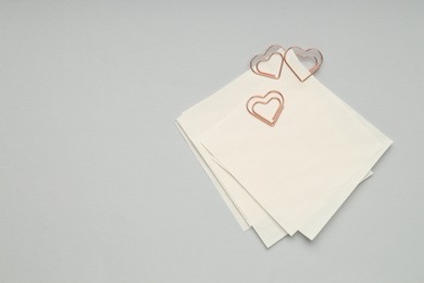 Photo of Heart shaped paper clips and notes on grey background, top view. Space for text