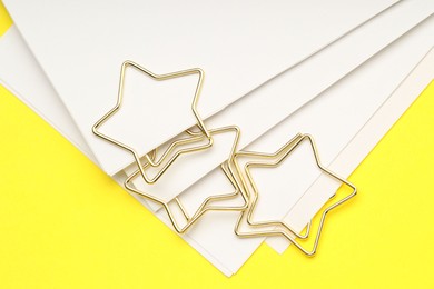 Photo of Star shaped paper clips and notes on yellow background, top view