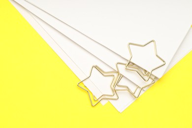 Photo of Star shaped paper clips and notes on yellow background, top view. Space for text