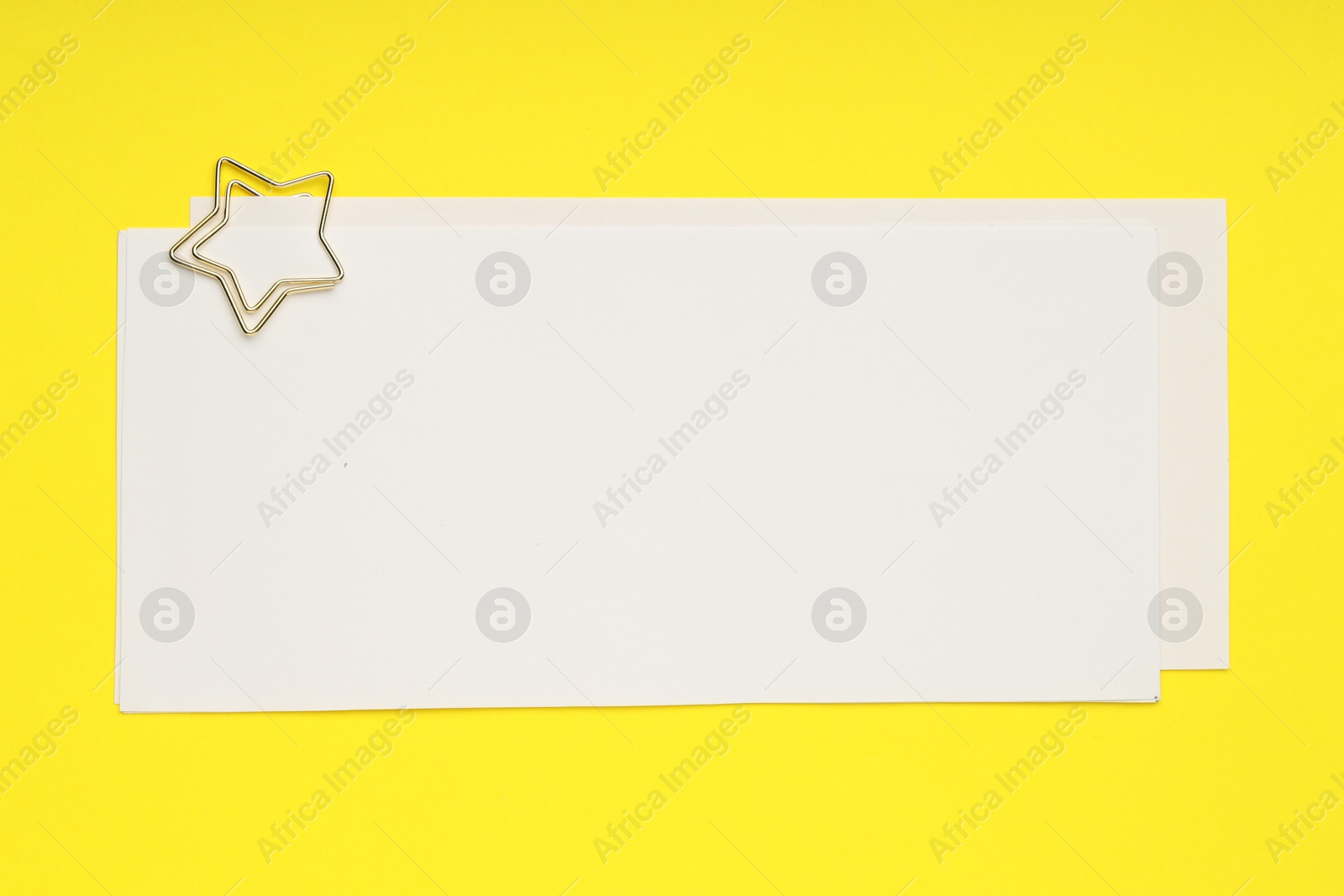 Photo of Star shaped paper clip and notes on yellow background, top view. Space for text