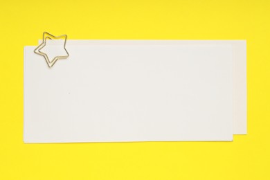 Photo of Star shaped paper clip and notes on yellow background, top view. Space for text