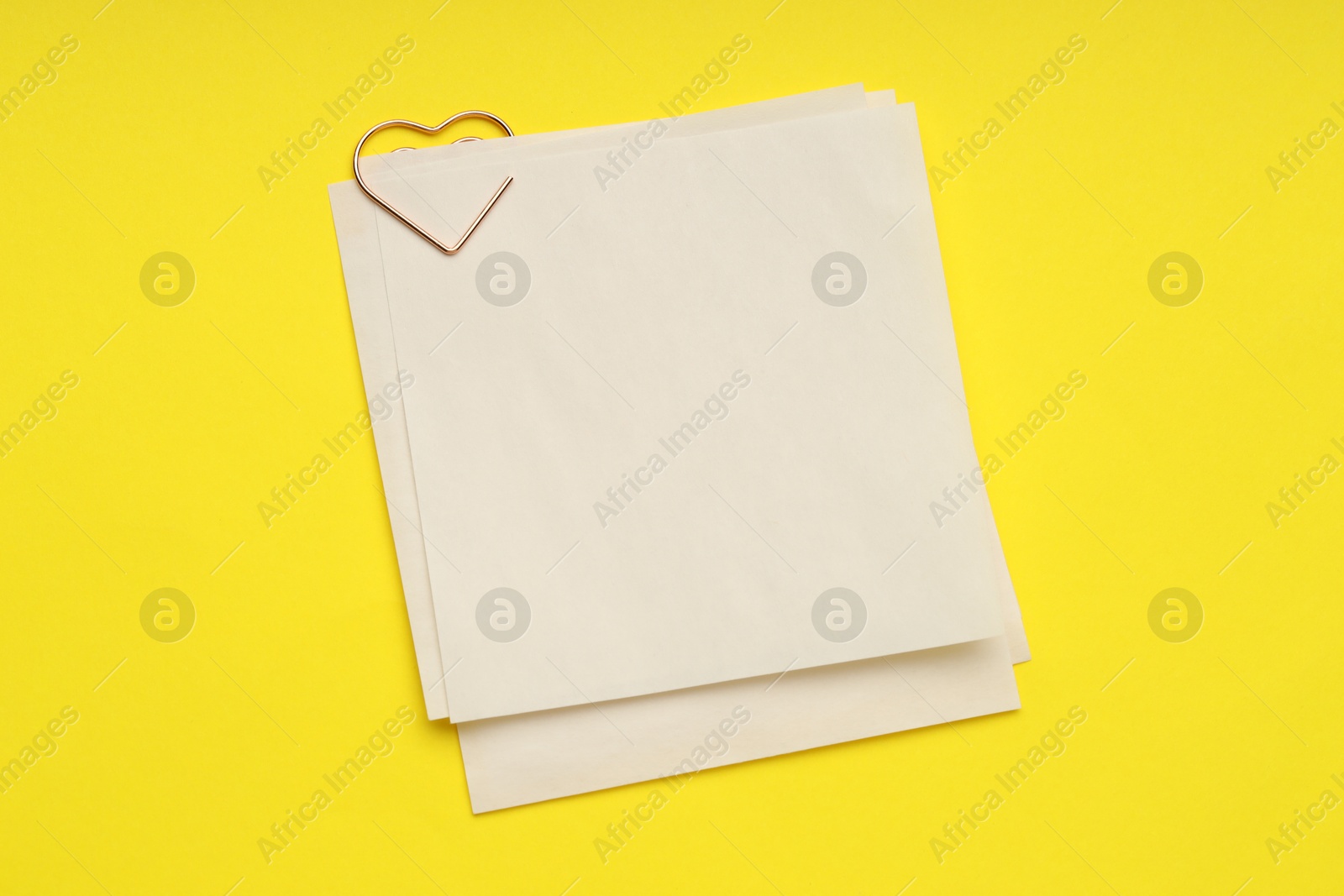 Photo of Heart shaped paper clip and notes on yellow background, top view. Space for text