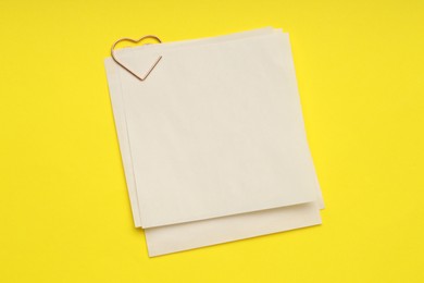 Photo of Heart shaped paper clip and notes on yellow background, top view. Space for text