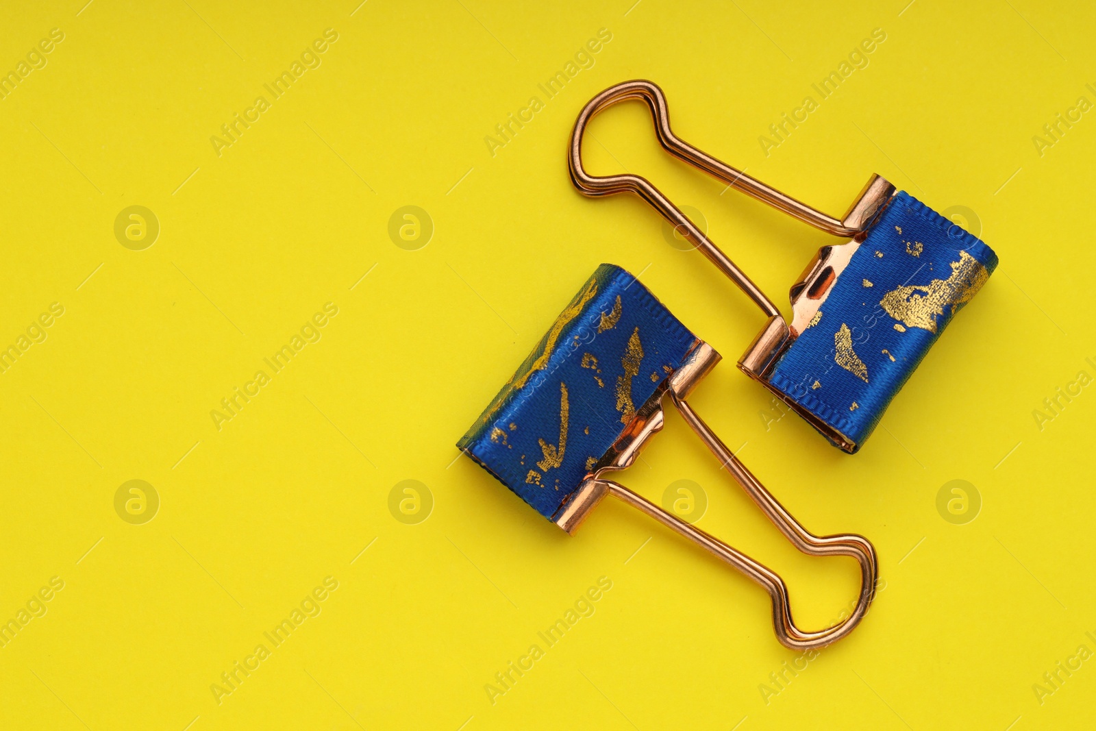 Photo of Two binder clips on yellow background, flat lay. Space for text