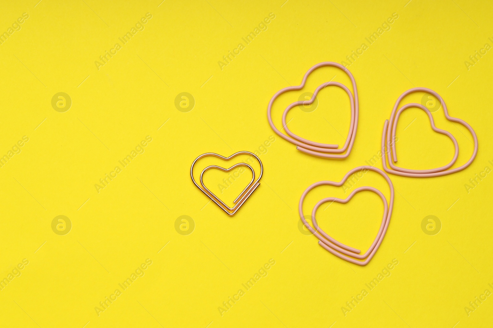 Photo of Heart shaped paper clips on yellow background, flat lay. Space for text