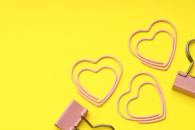 Photo of Heart shaped paper and binder clips on yellow background, flat lay. Space for text