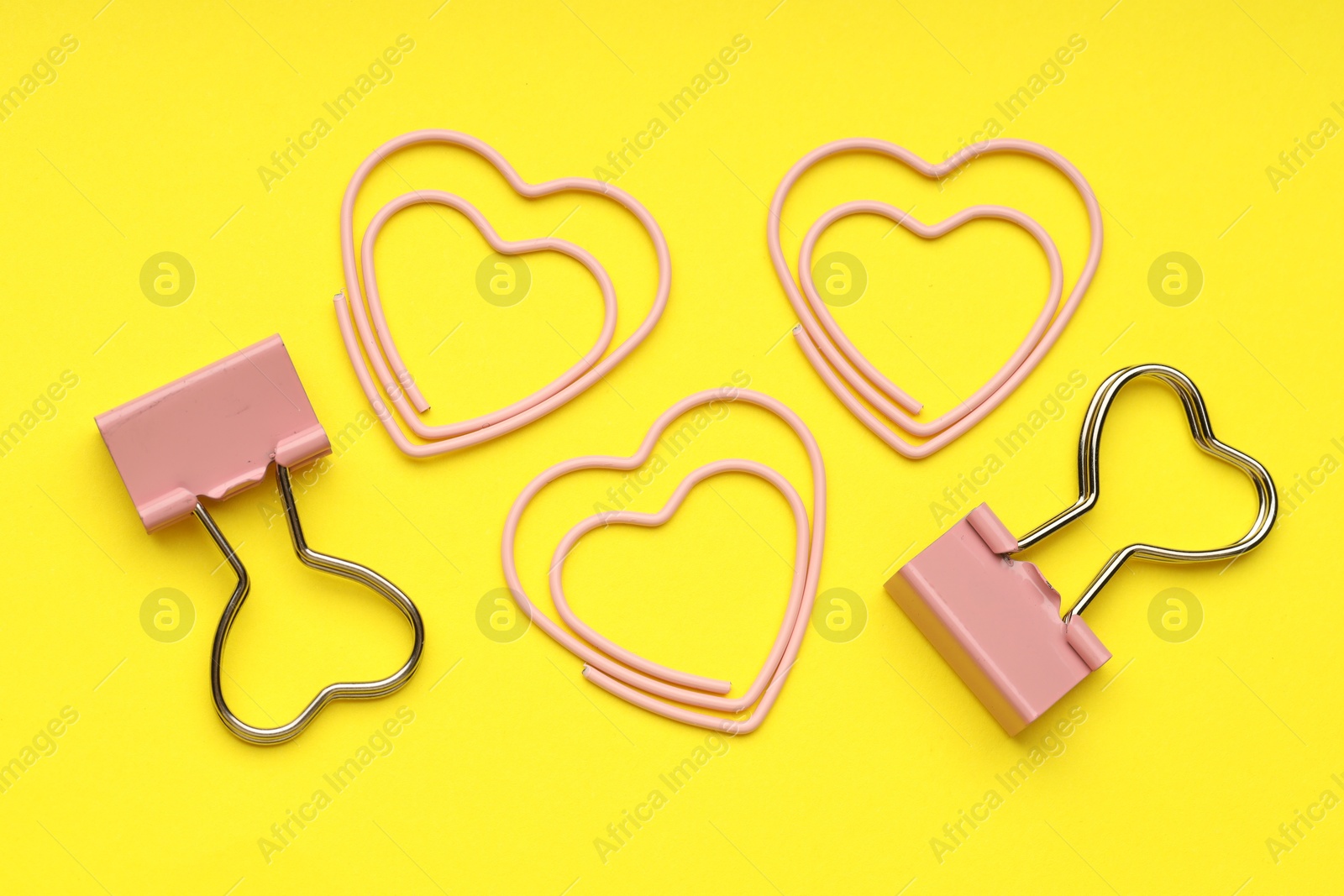 Photo of Heart shaped paper and binder clips on yellow background, flat lay