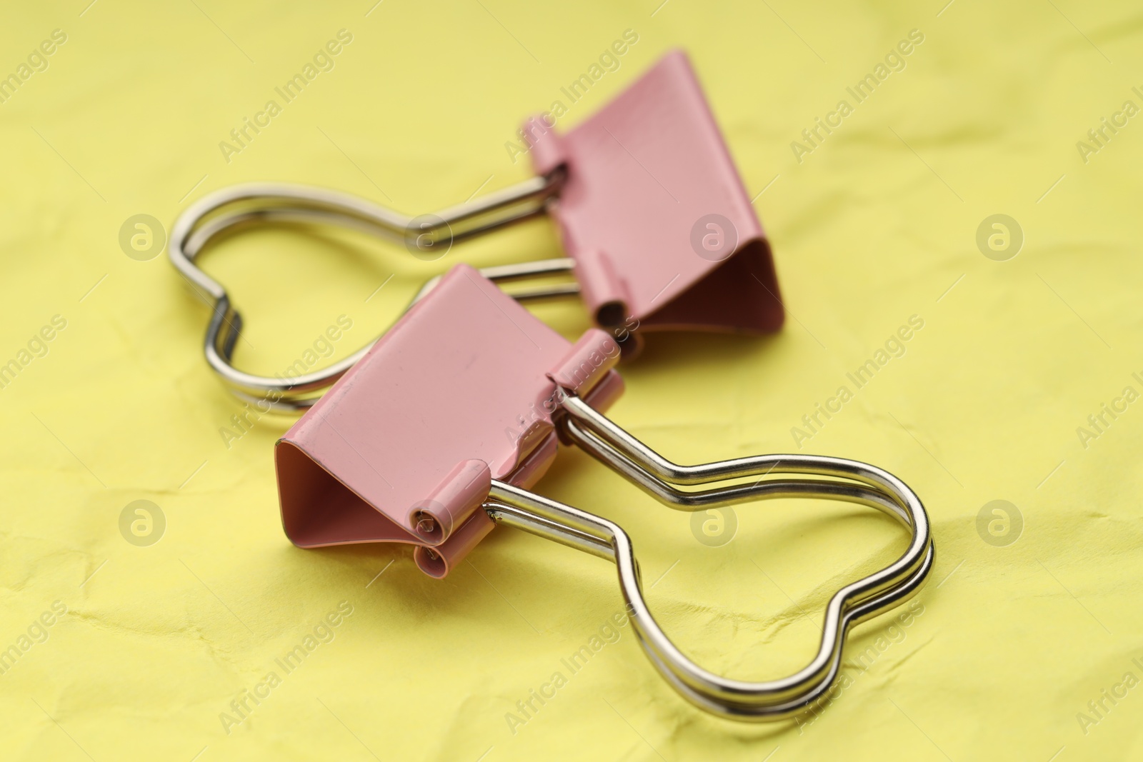 Photo of Beautiful binder clips on crumpled yellow paper, closeup