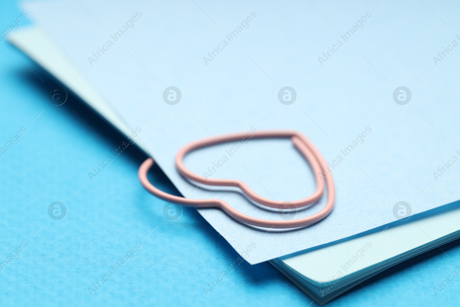 Photo of Heart shaped paper clip and notes on light blue background, closeup